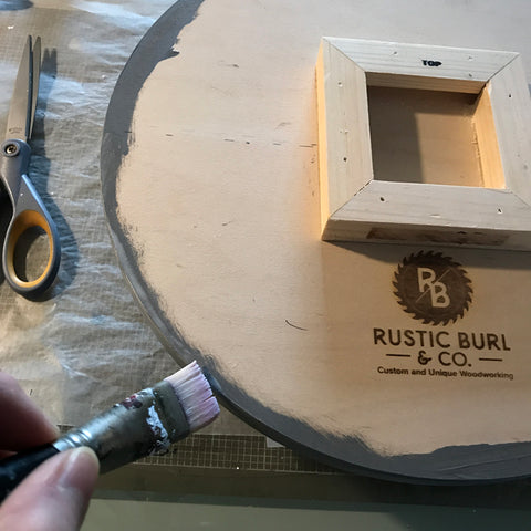 hand holding brush applying glue to side of wooden circle