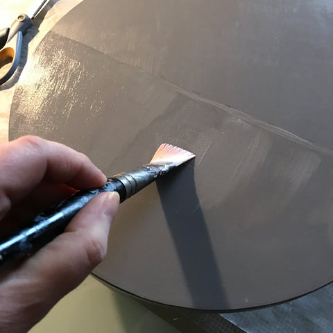 Hand holding brush applying glue to wooden panel