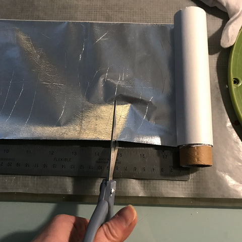 Hand holding scissors cutting a section of metal leaf