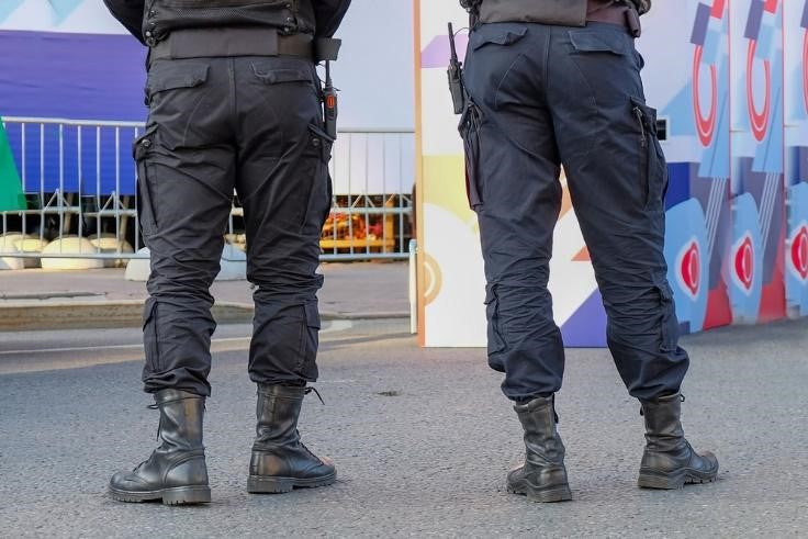 Back view of police officers wearing cargo pants near steel barricade