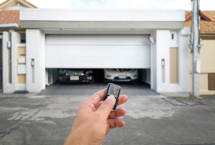 Hand holding a remote control in front of a garage door with two cars inside