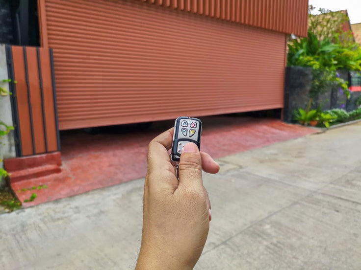 Hand holding remote control to open red garage door