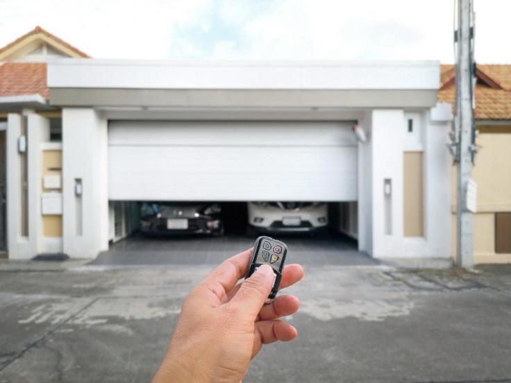 Hand holding remote control to open white garage door