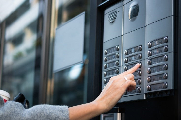 Woman pressing code on intercom of residential building