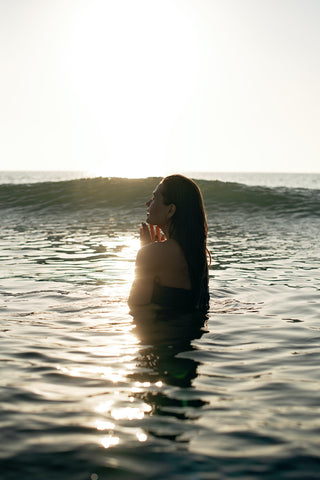 woman in water with hands near chest and sun glistening all around her