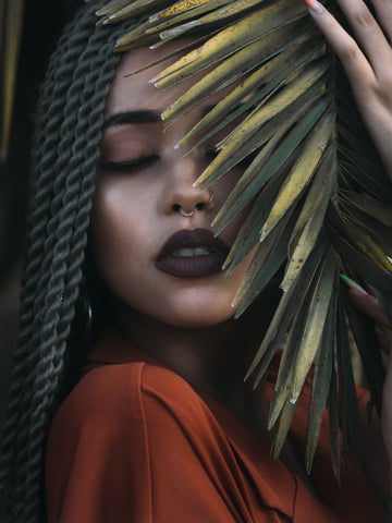 Multiracial woman with braids in her hair has a bush over her face and eyes closed.