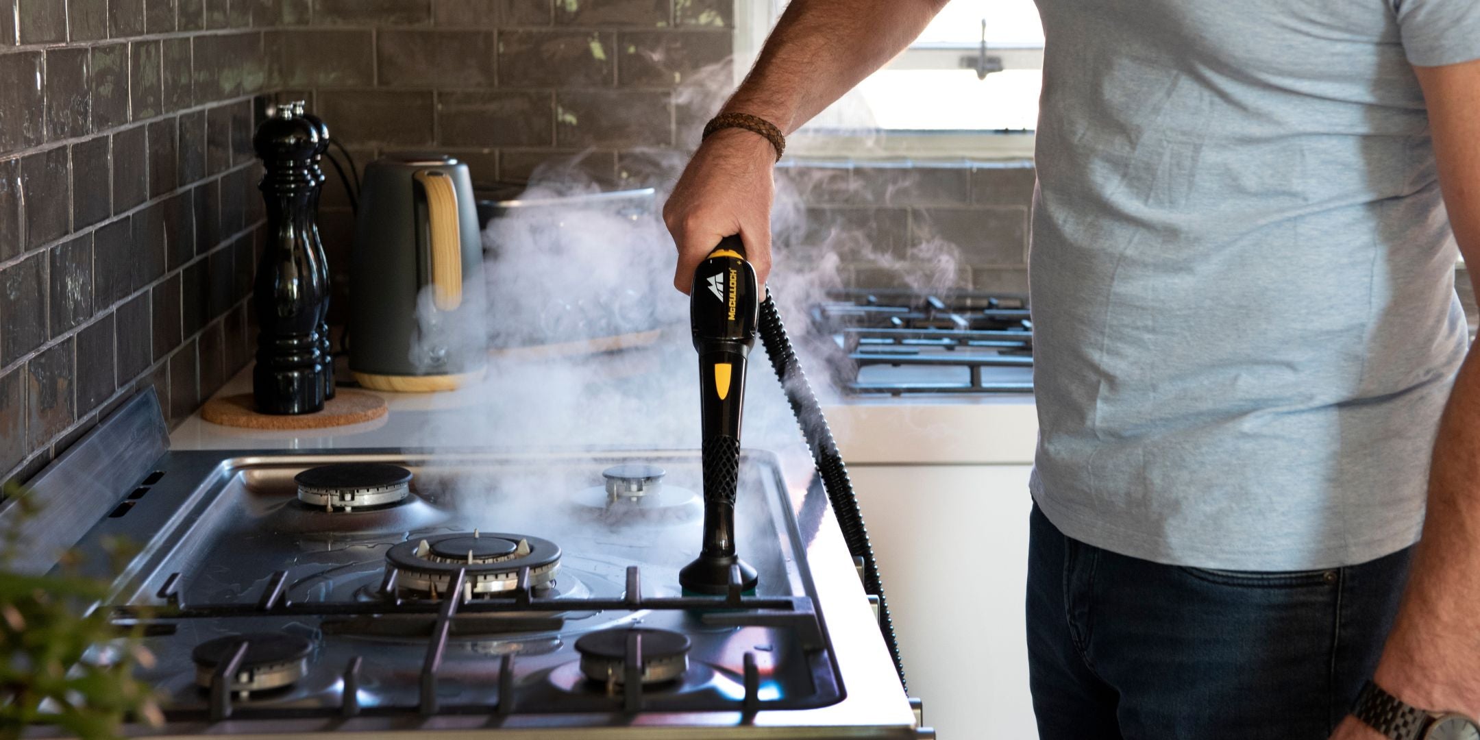 Man using High Pressure McCulloch Steam Cleaner to clean stove top using round sponge attachement.
