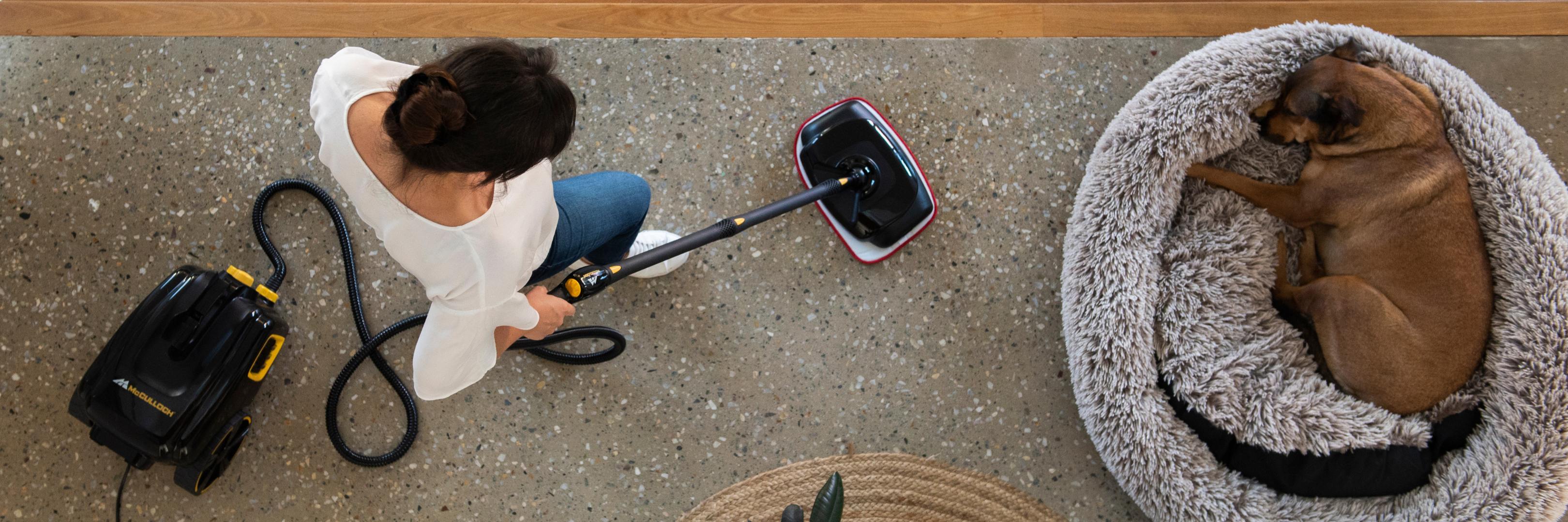 Woman using McCulloch Steam Cleaner to steam clean floors around a dog who is sleeping in his bed.