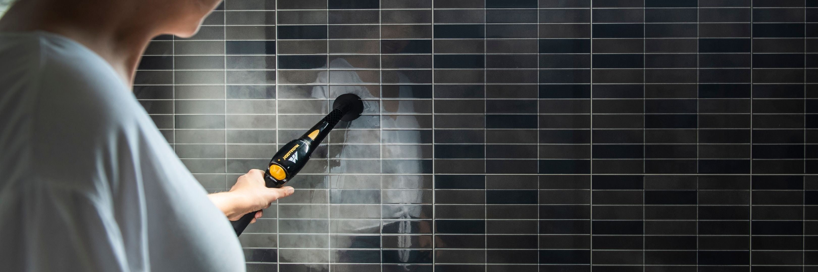 Woman cleaning bathroom wall tiles with McCulloch Steam Cleaner.