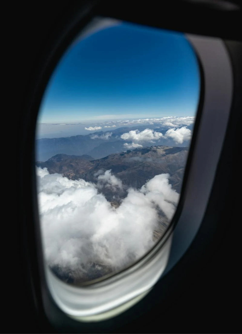 View from airplane window, overlooking onto blue skies, mountains and clouds