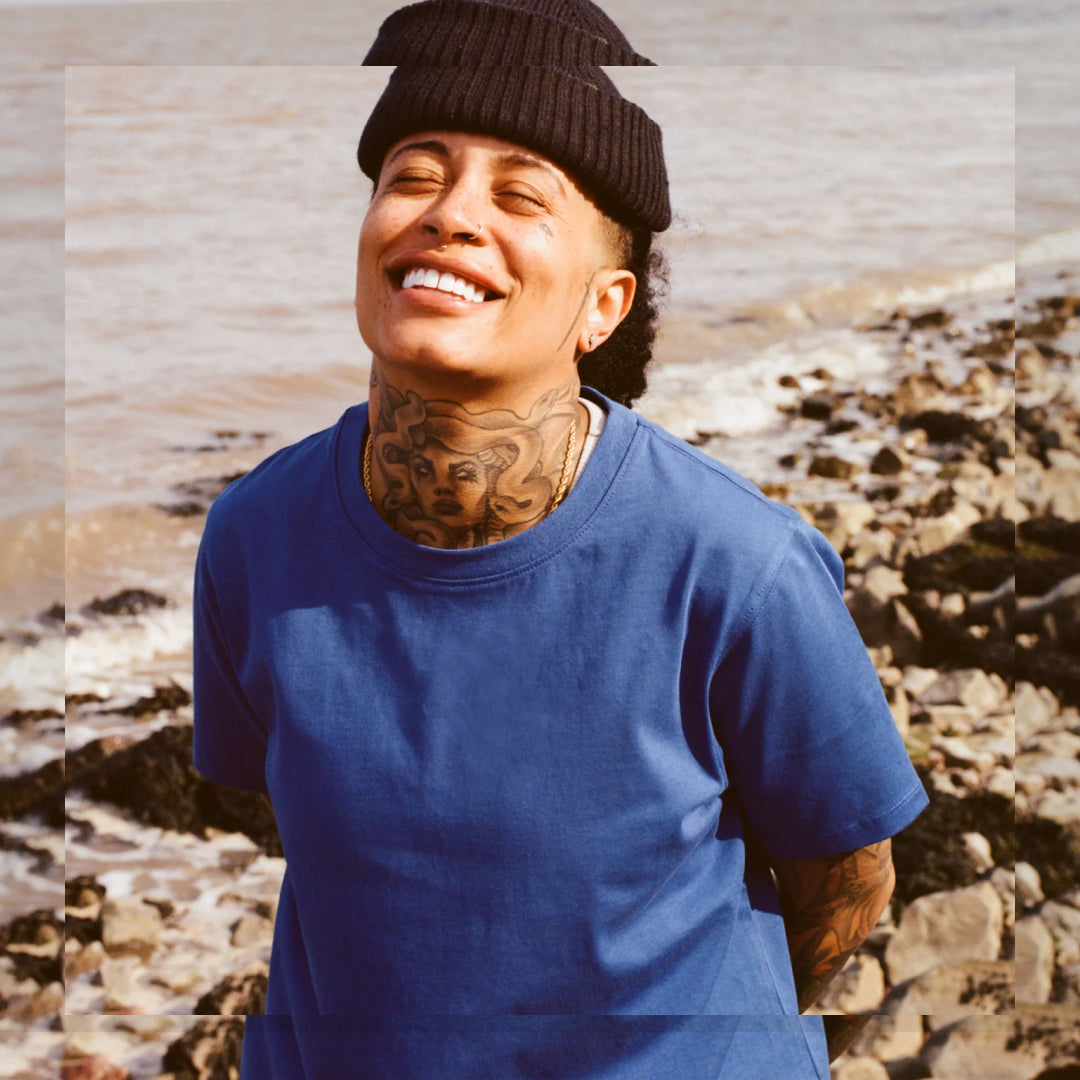 Transmasc person in blue shirt and beanie, smiling with eyes closed