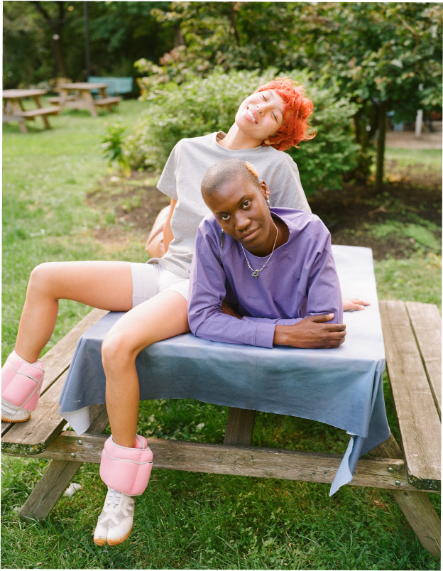 Two nonbinary folks sitting on a picnic table outdoors at a park