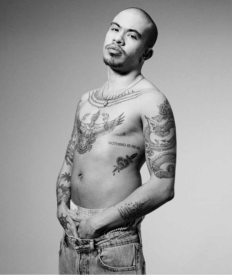 Transmasc person with shaved head and tattoos, shirtless, wearing jeans
