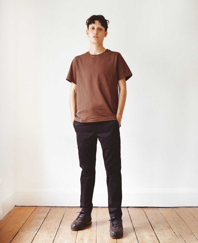 Nonbinary model wearing brown tee and black Marlo pants