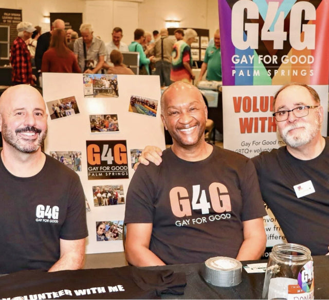 Three volunteers sitting in front of a pride flag that says G4G, at a donation table for Gay For Good.