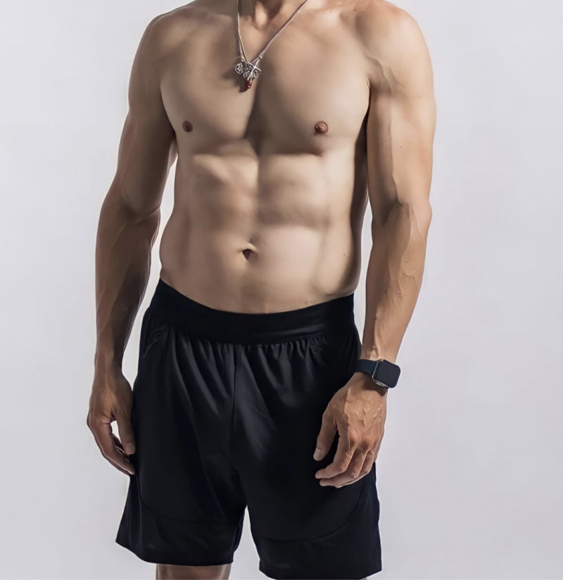 Shirtless individual with baggy black swim trunks on