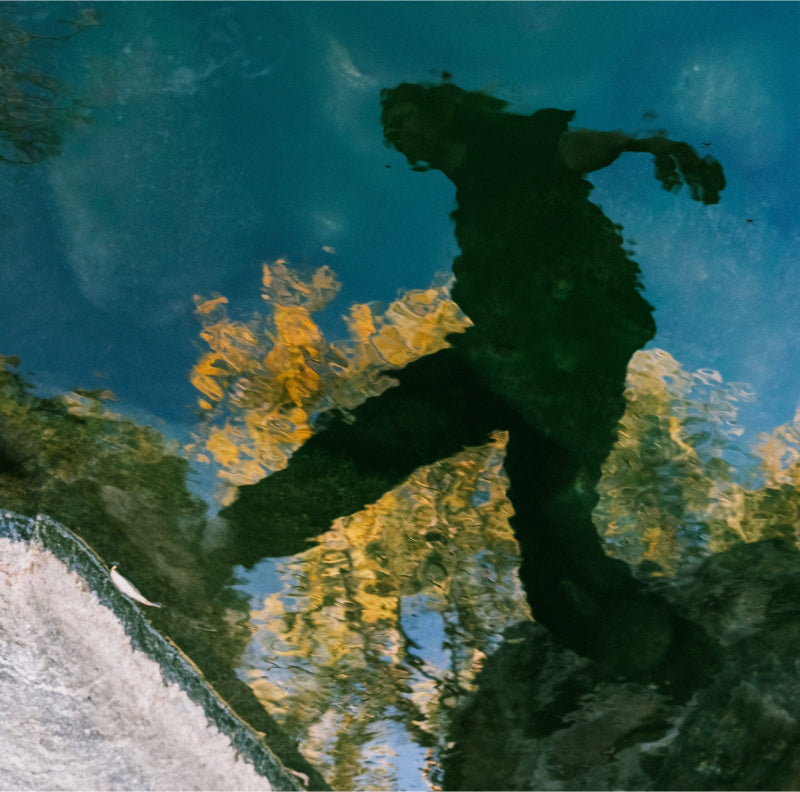 Photo of a reflection in the river, of a person jumping on stepping stones