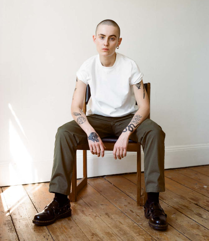 Model in white t-shirt and olive green Marlo pants, sitting on chair