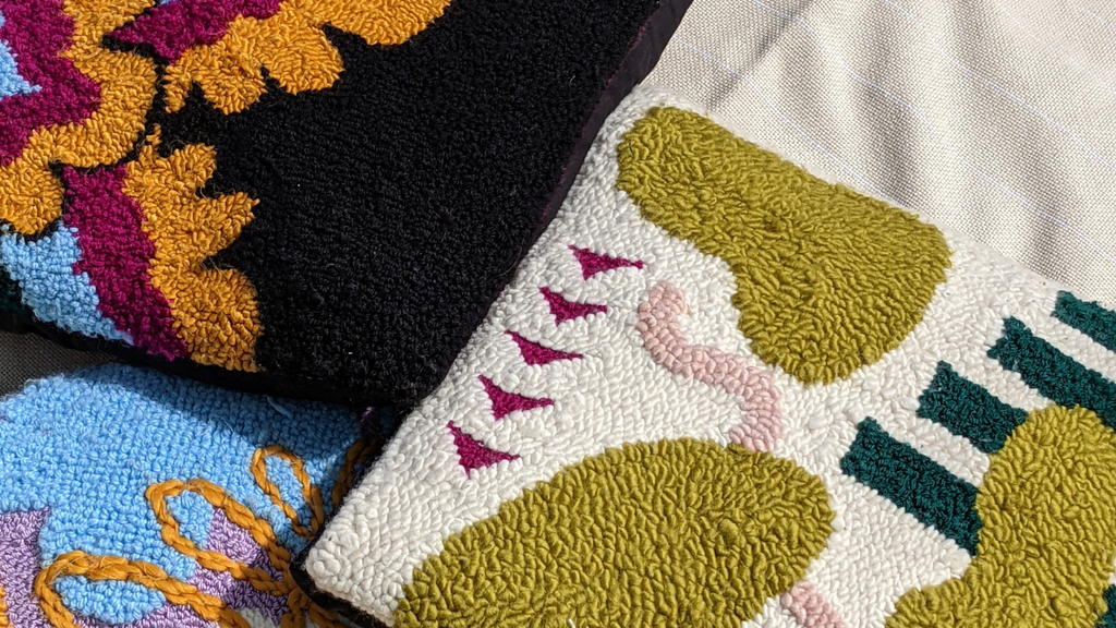 This is a close-up image of three different punch needle pillows in a loose pile. One pillow features an 18th-century inspired design, one features a geometric blob design, and one features and abstract floral design. dancing arms punch needle embroidery, handmade in Los Angeles, California.