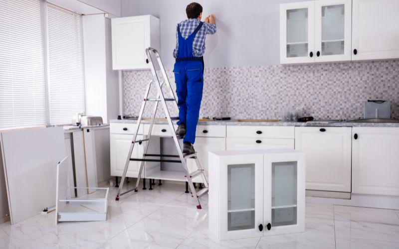 Carpenter Assembling Cabinet On Wall In Kitchen