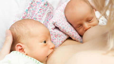 Mother breastfeeding twins in double rugby ball hold