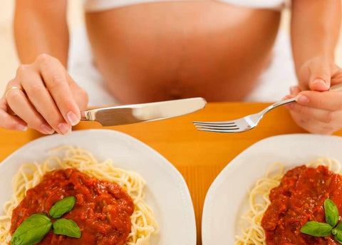 Pregnant woman eating two plates of spaghetti as part of nutrition in pregnancy blog on Be Active Maternity and nursing activewear site.