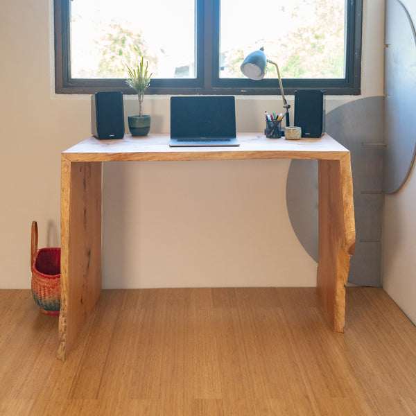 A waterfall style live edge desk is set up as an office work desk, complete with laptop, two speakers, a desk lamp, and potted plant. Located at the JOHI office, this desk is made of Santa Cruz grown Monterey Cypress.