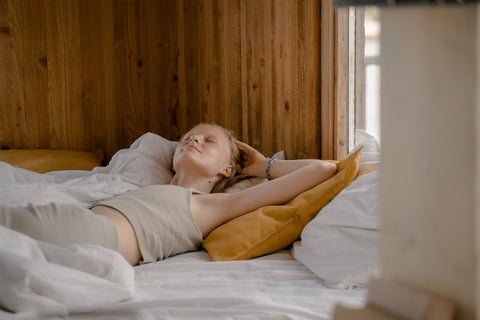 A woman stretching after waking up in a bed next to a wooden wall.