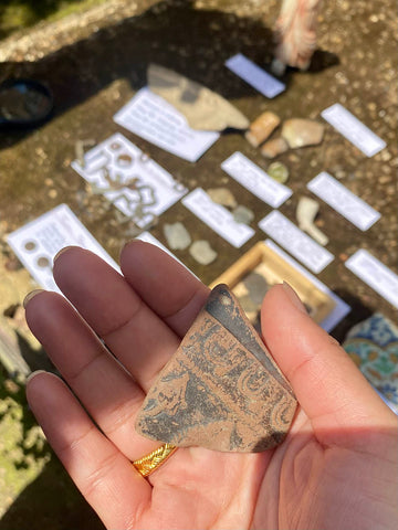 A hand holding a fragment of blackened samian ware pottery, found in the River Thames