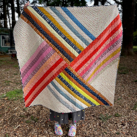 Shannon holds up an Adventureland quilt in reds, blues, browns and naturals