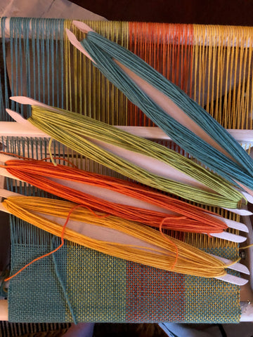 a rigid heddle loom from above, with 4 shuttles wound with different colors of yarn