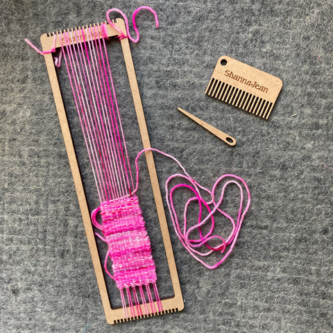 a wooden bracelet loom warped with hot pink yarn, with accessories next to it