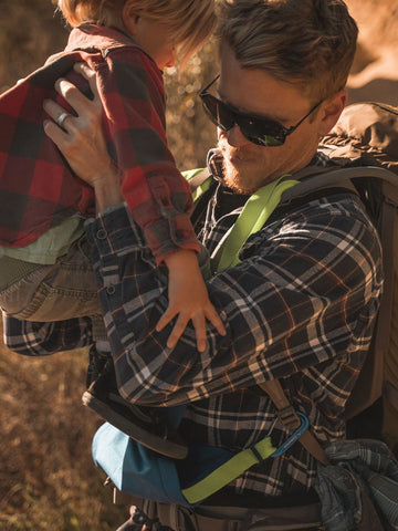 A man getting a child in a Trail Magik child carrier while exploring outdoors