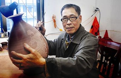 Li Changquan carving a design on a nixing clay vase