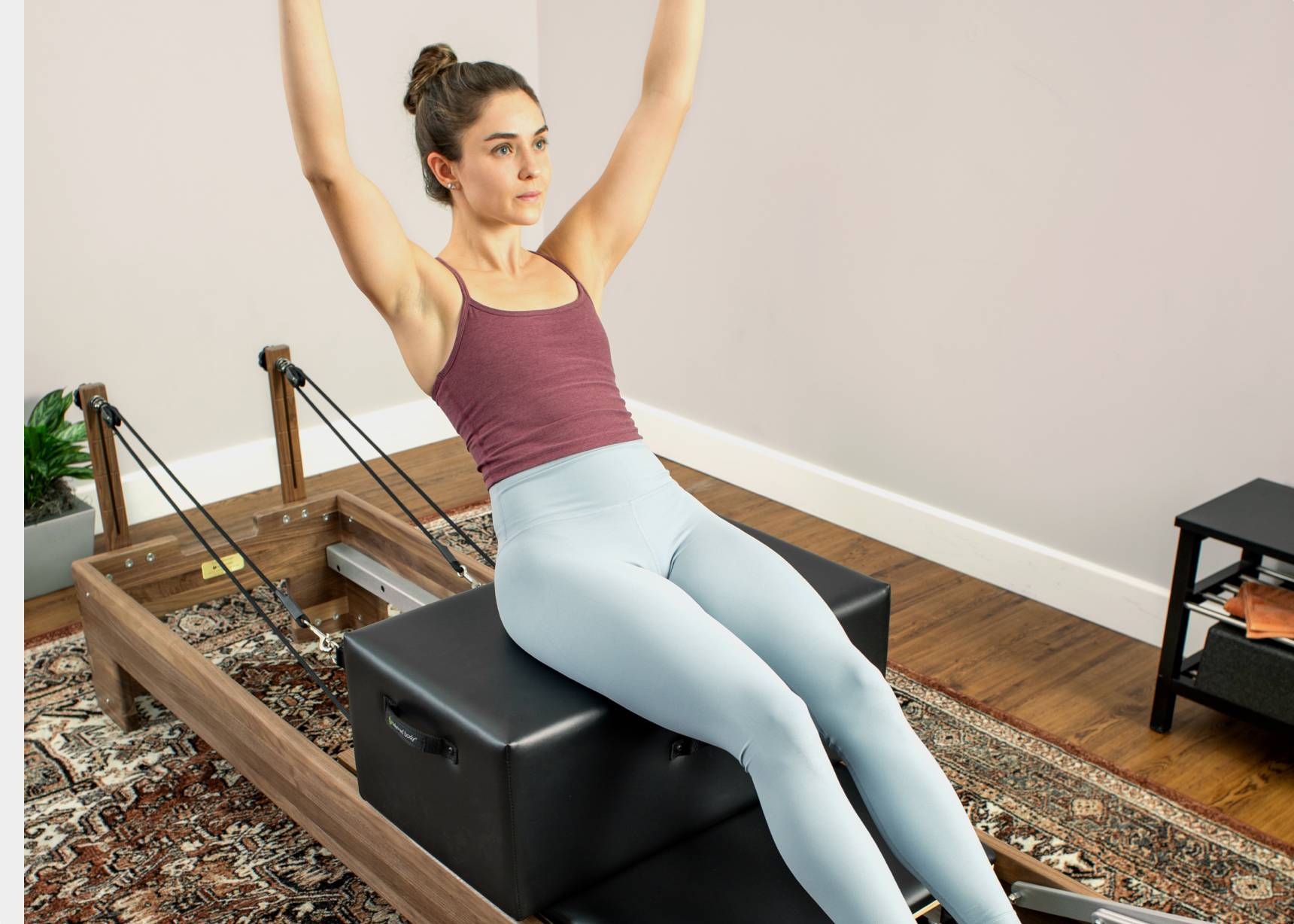 Woman seated on New York-style Pilates reformer box.