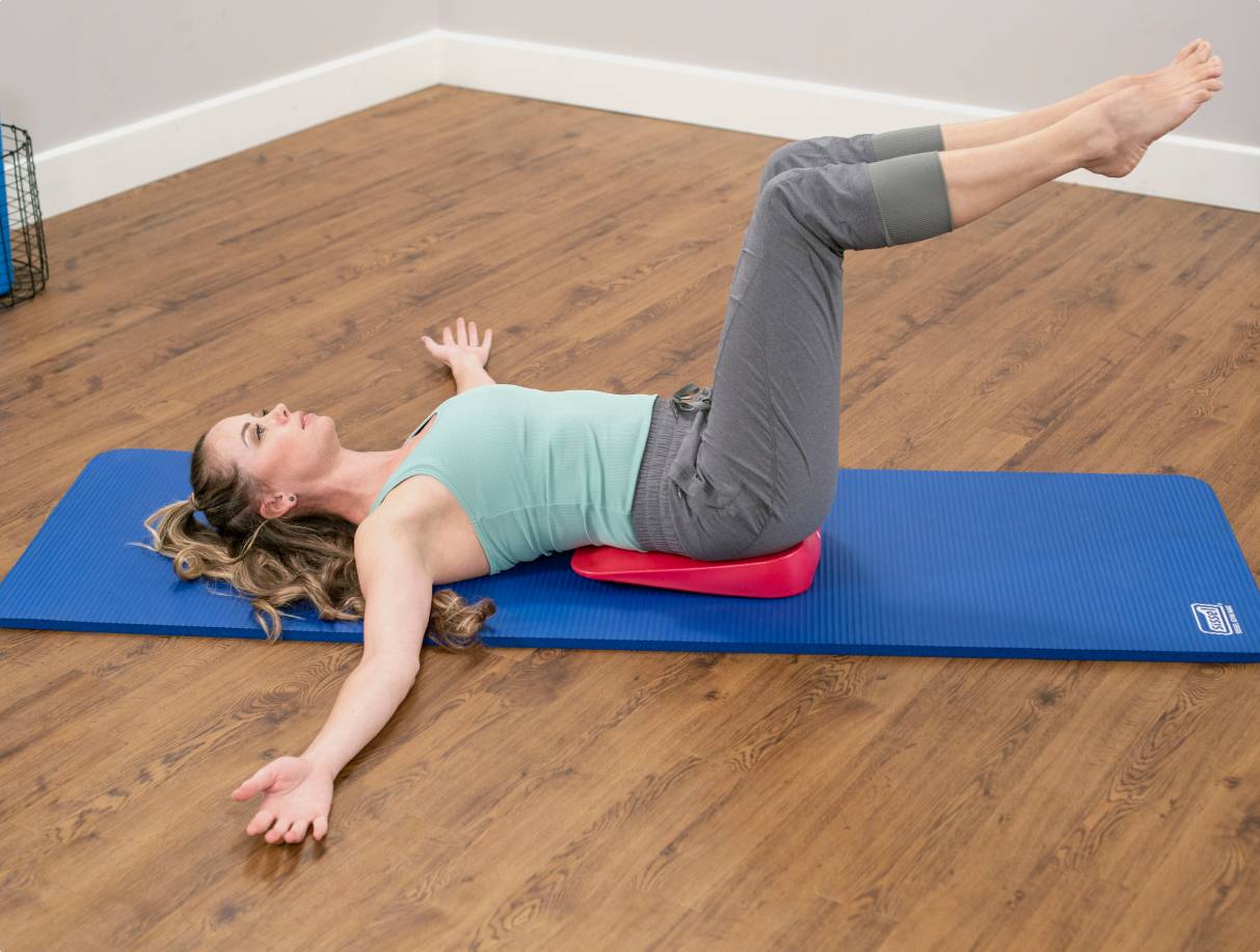 Woman lying on red inflatable wedge on blue mat.