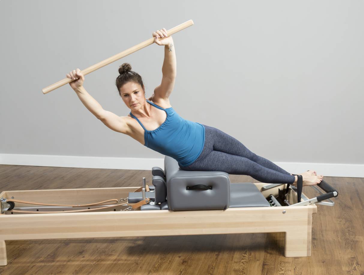 Woman using a maple dowel on a reformer with a sitting box.