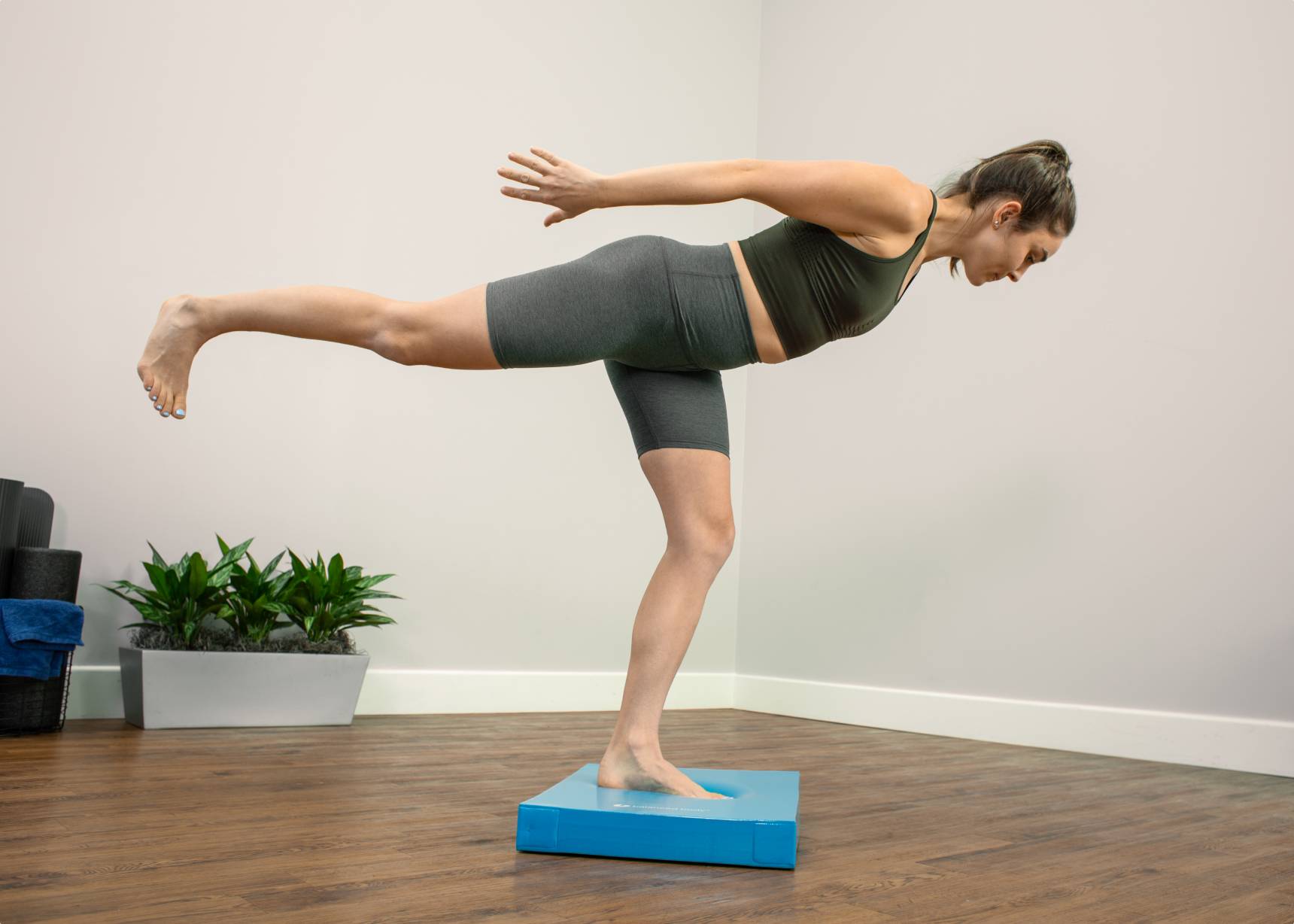 Woman performing a one-leg stand on a blue Balance Pad.