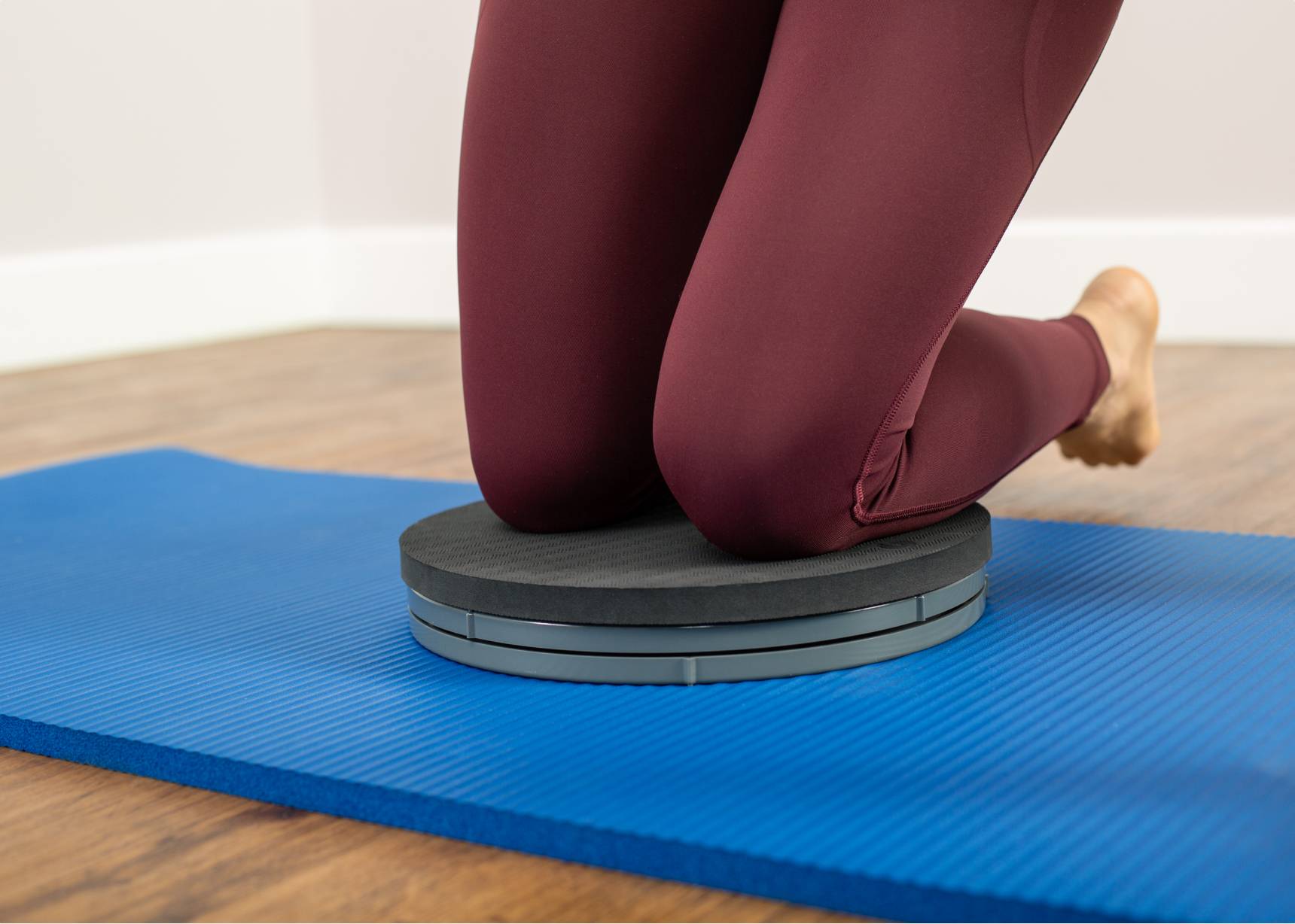 Individual kneeling on a Rotator Disc pad with both knees engaged in a pilates exercise.