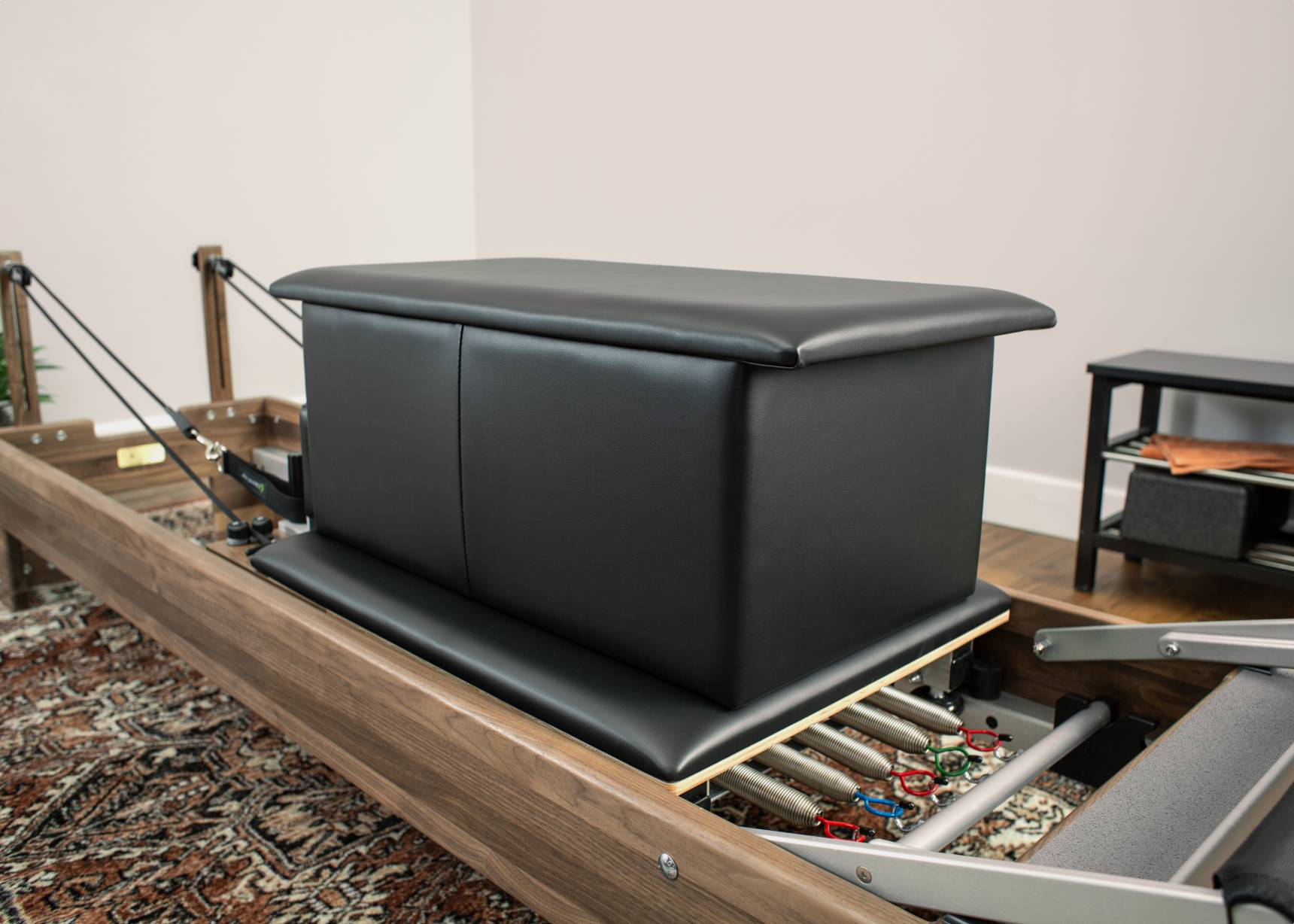 A black large sitting box placed on a reformer, featuring signature springs in the background.