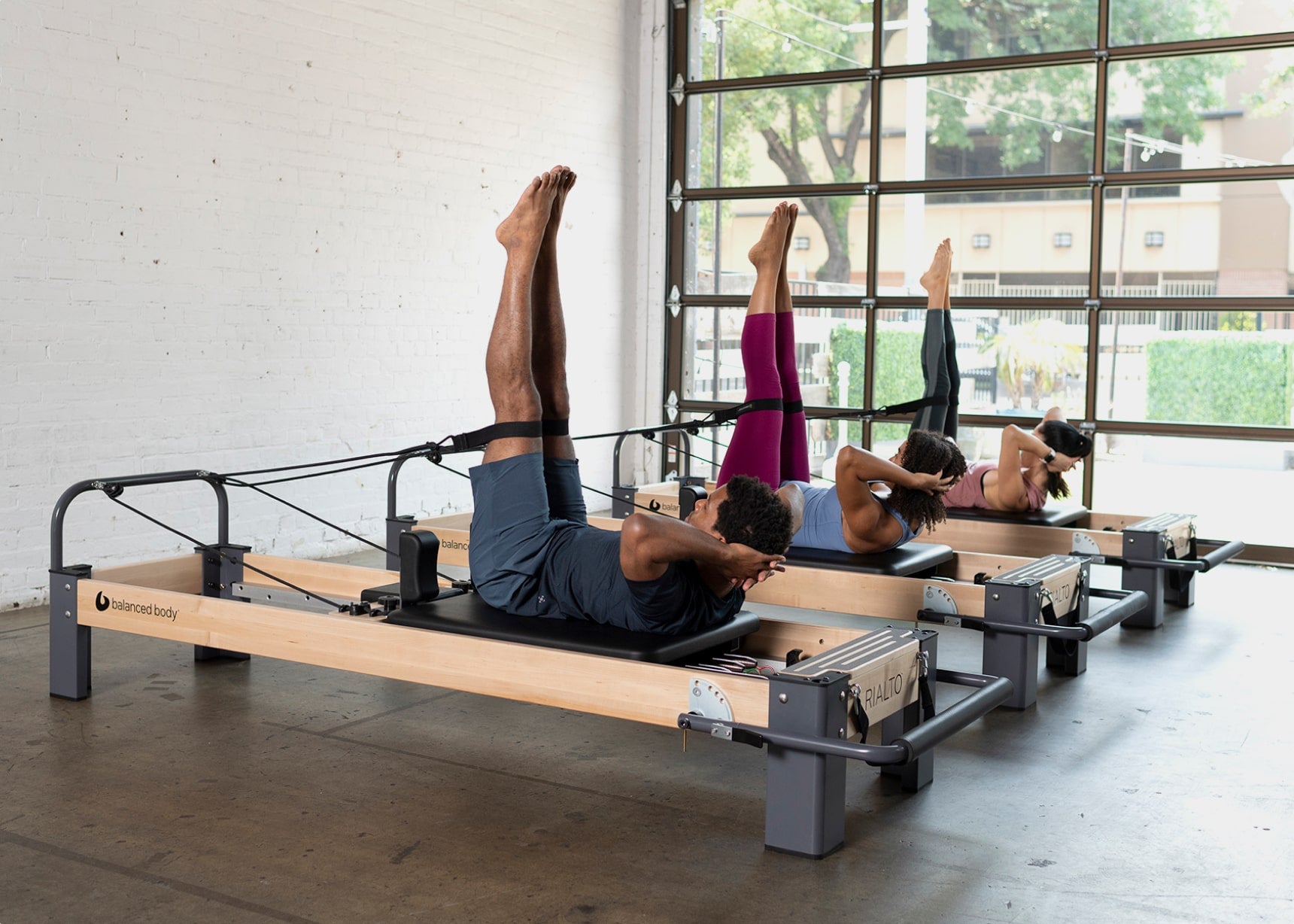 3 Pilates students laying on Reformers with legs in loops and extended in the air