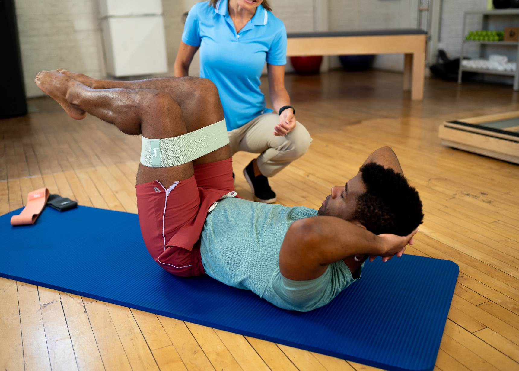 A man stretching his arms and torso using a resistance band on a blue exercise mat.