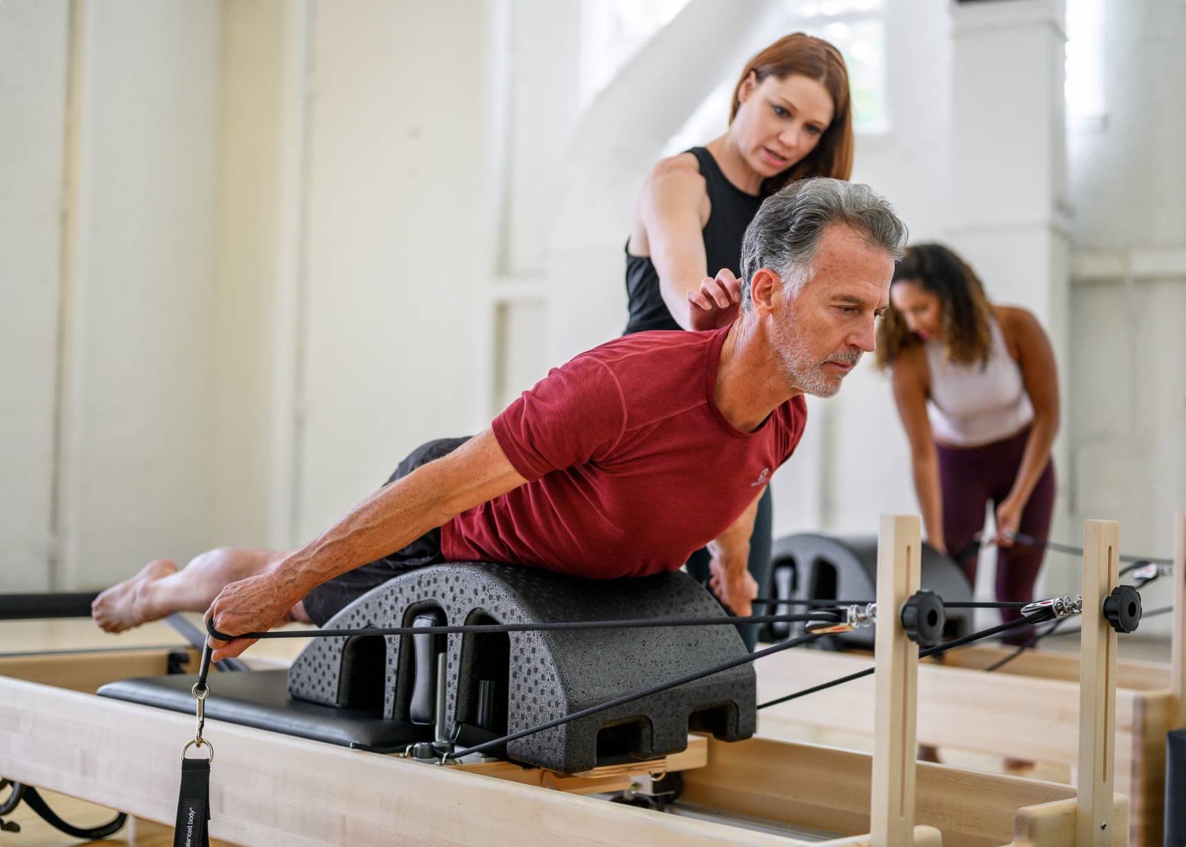 Pilates instructor assists client using the Pilates arc while extending limbs on a reformer