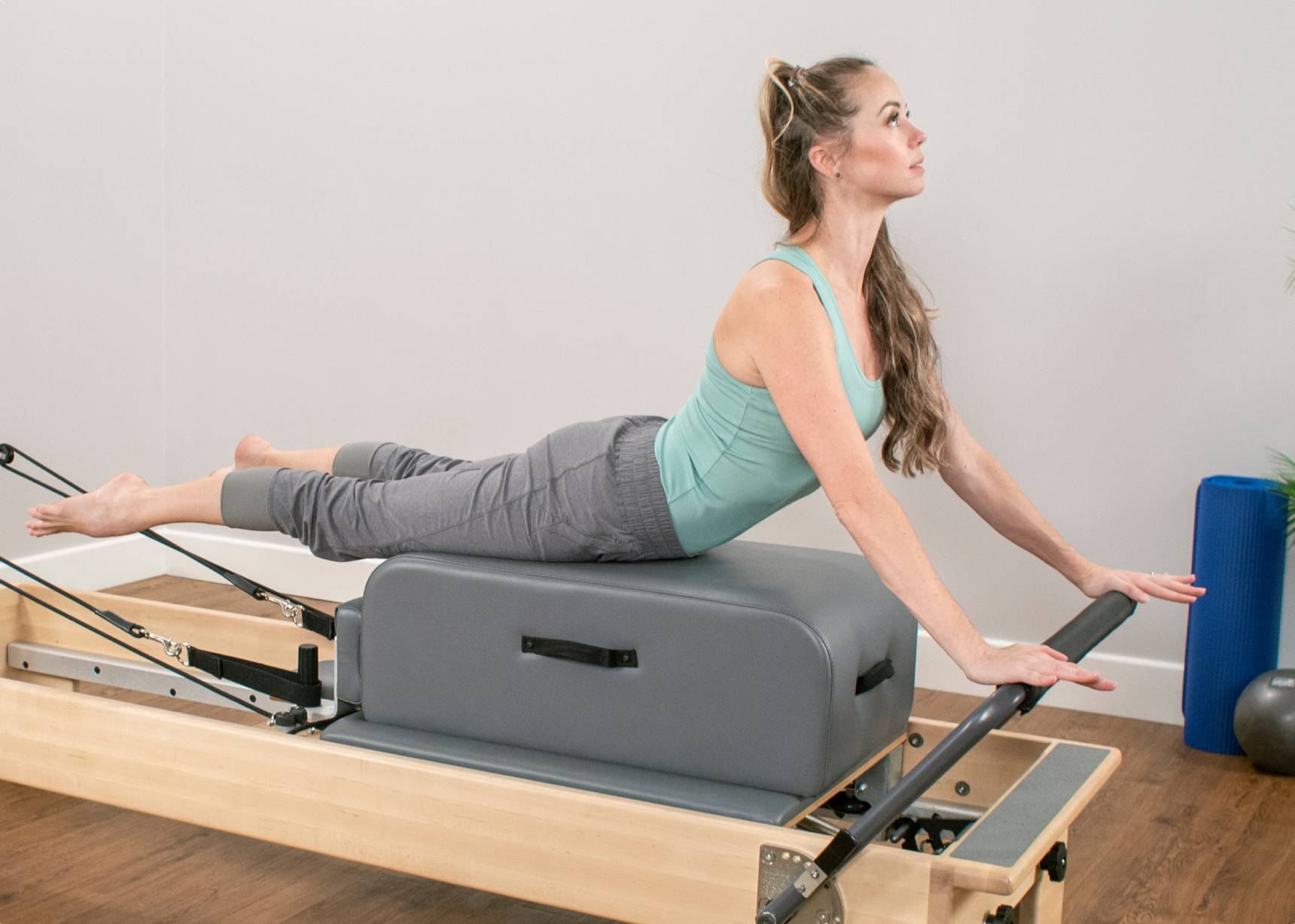 A woman leveraging a contour sitting box for enhanced stability while on a reformer.