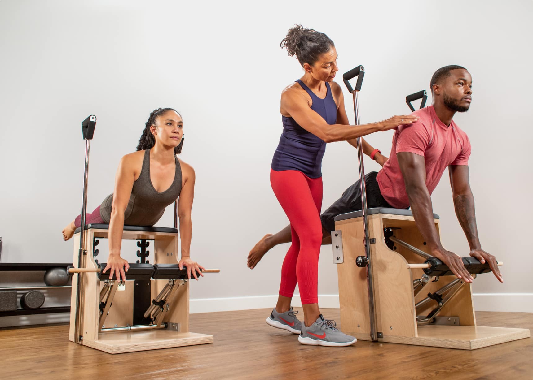 Pilates instructor assisting clients pushing their chest up while laying pelvis across a Pilates chair