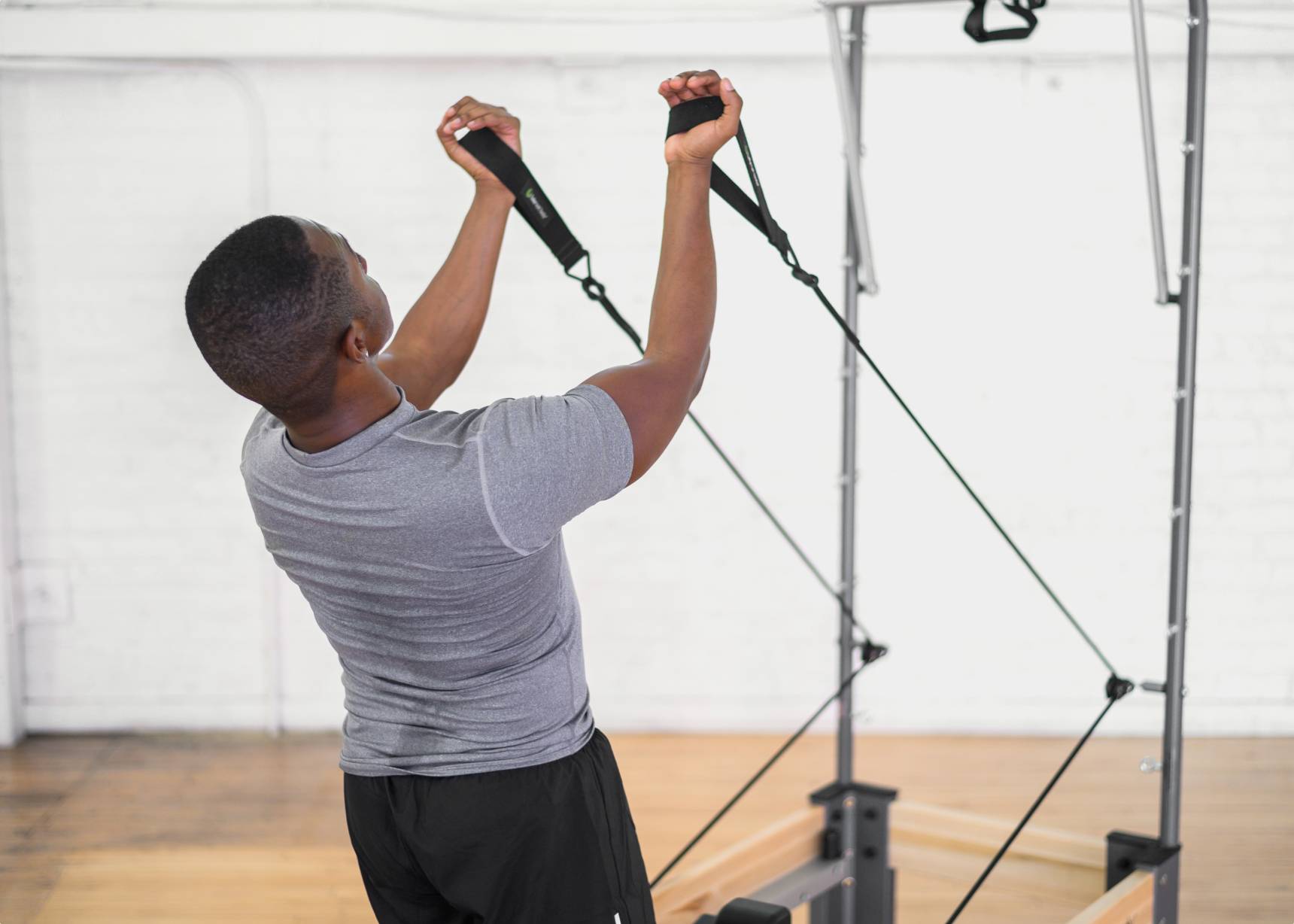 A man intensively working out by pulling on loops attached to a Pilates tower.