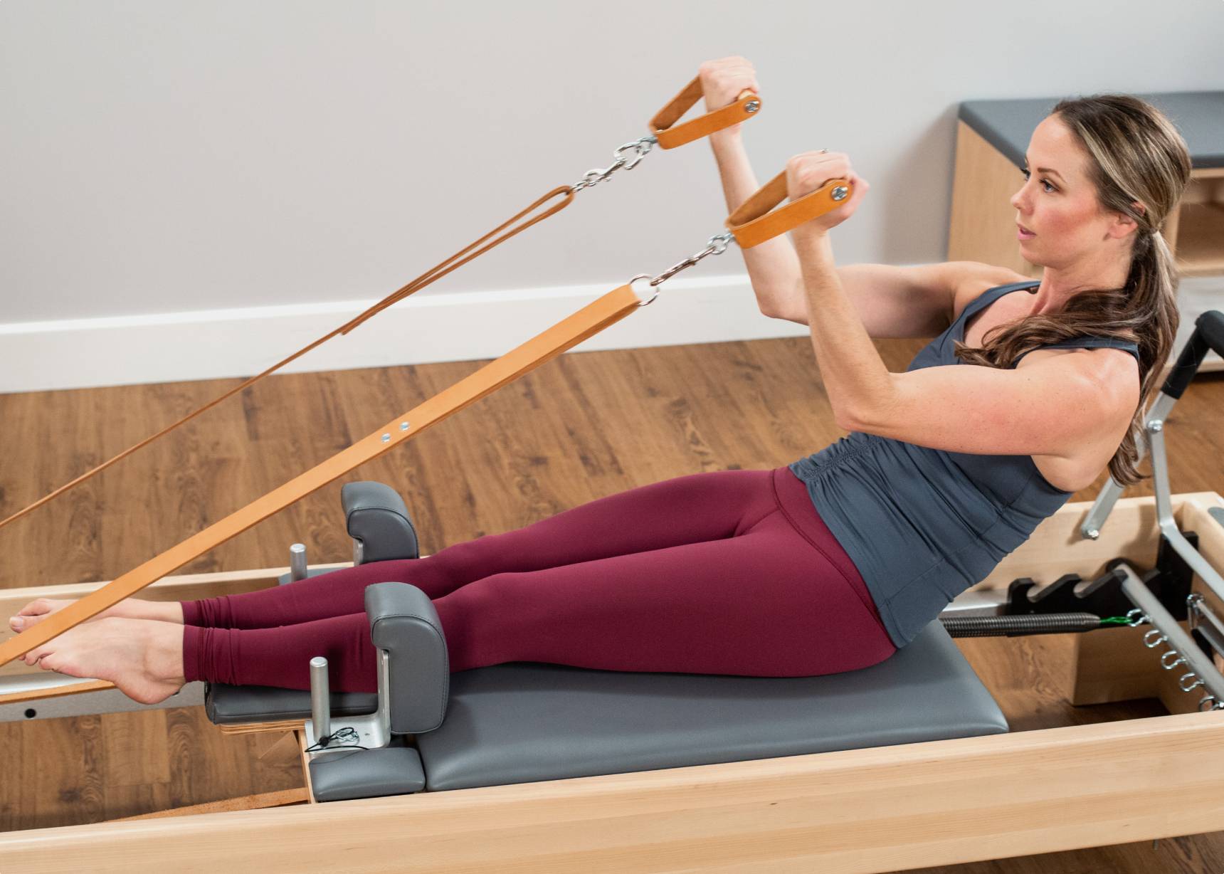 Woman pulling leather straps attached to an Allegro Reformer.