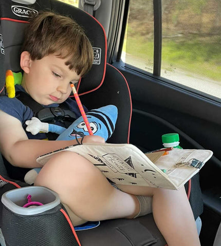 Child drawing in their car seat on a road trip