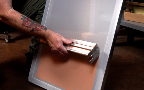 person coating a screen with pink emulsion