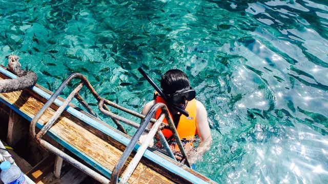 A man in a life vest and snorkel gear holding onto the ladder on the side of a boat in the ocean